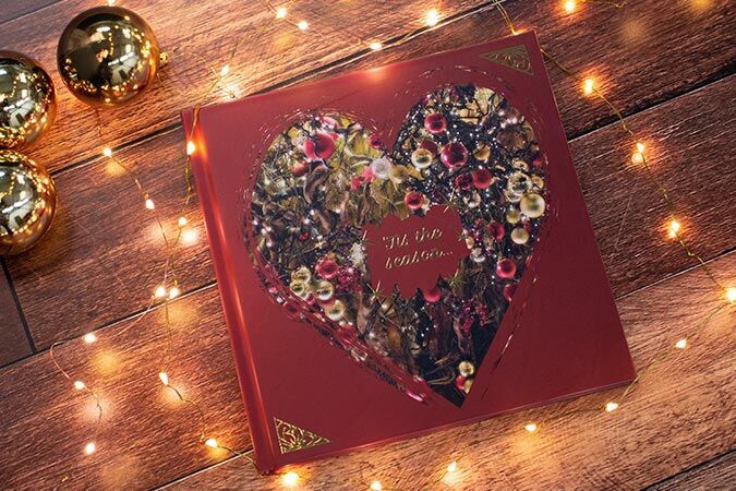 Red heart-shaped photo book with festive design, surrounded by lights and gold ornaments