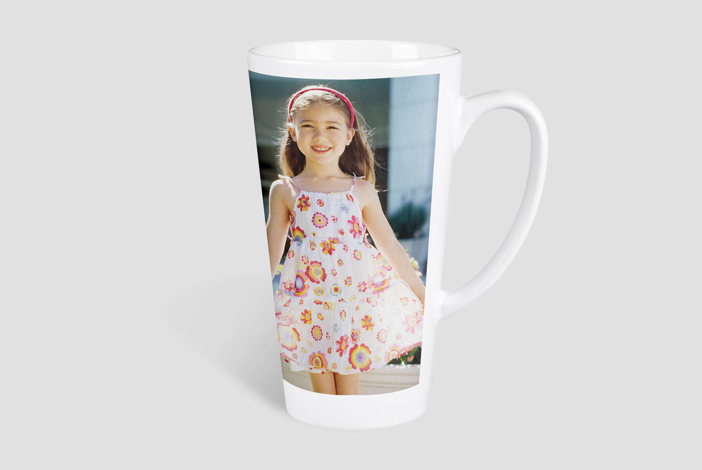 A white mug with a colorful photo print of a girl in a dress with flowers. The mug is in a bright setting.