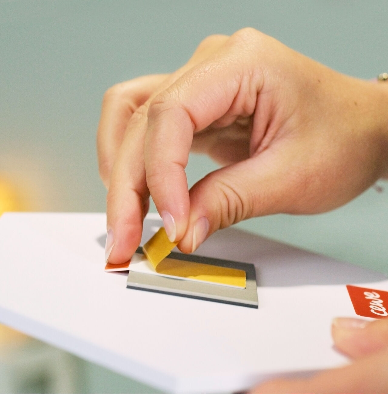 A hand applying a yellow piece of paper to a greeting card.