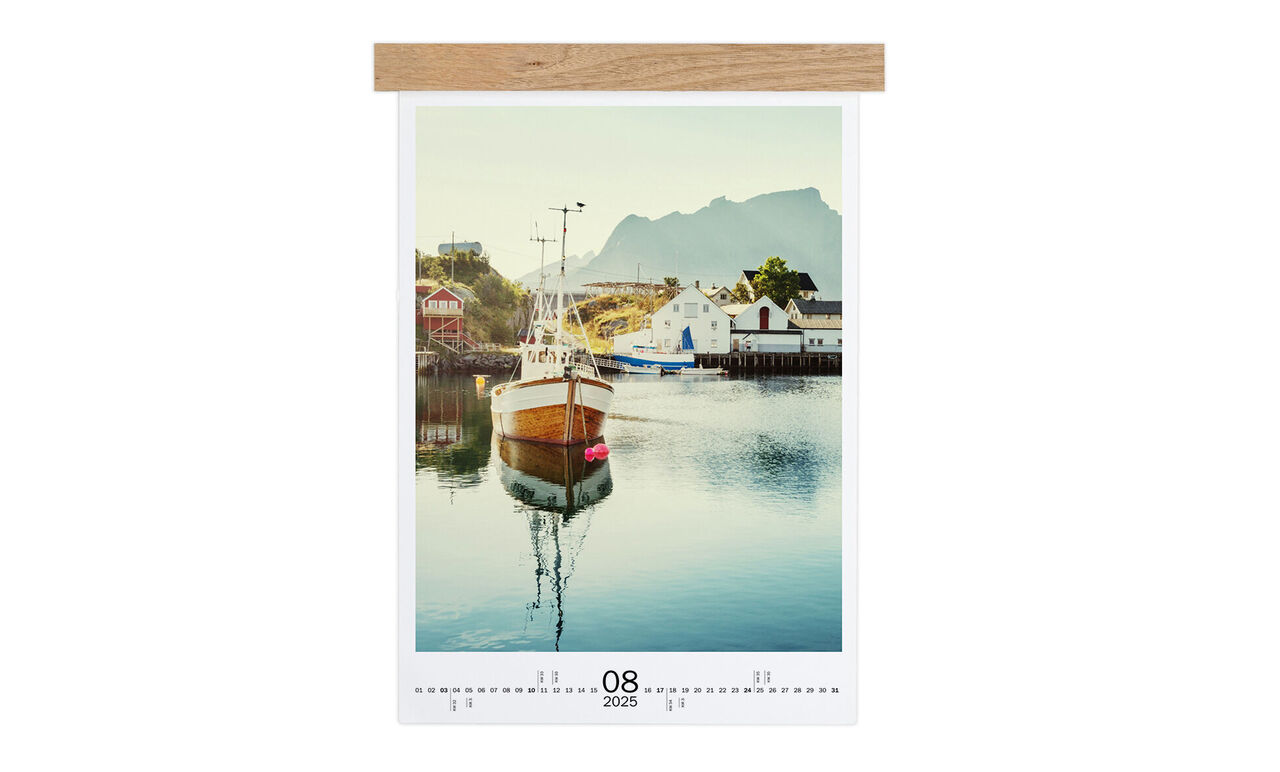 A pretty boat rests quietly in the harbor with mountains in the background. It’s a sunny day.