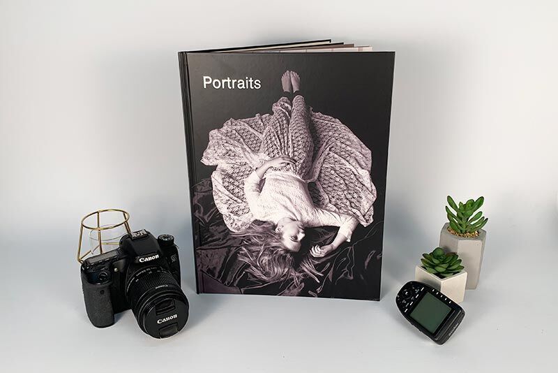 Black photo book titled 'Portraits' lying on a table next to a camera and plants.