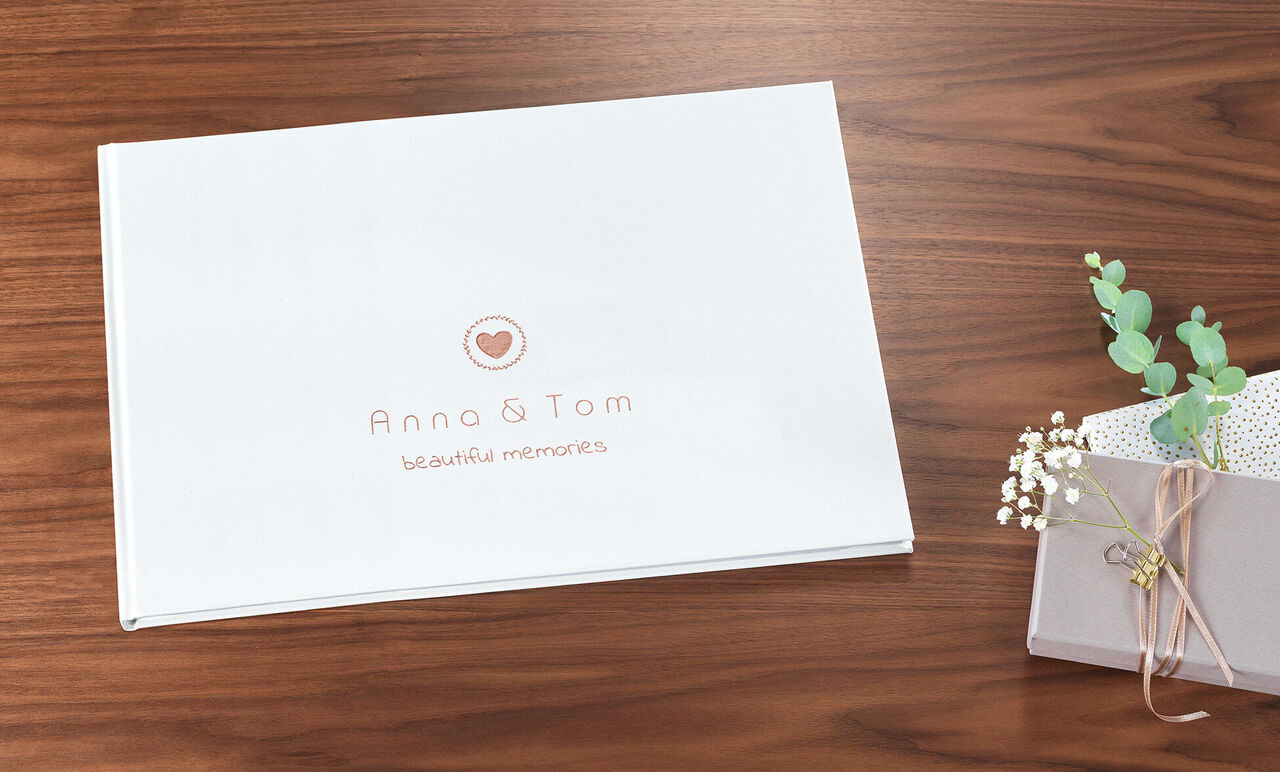 A lovingly designed CEWE PHOTOBOOK titled 'Anna & Tom beautiful moments' on a wooden table, next to a small flower pot.