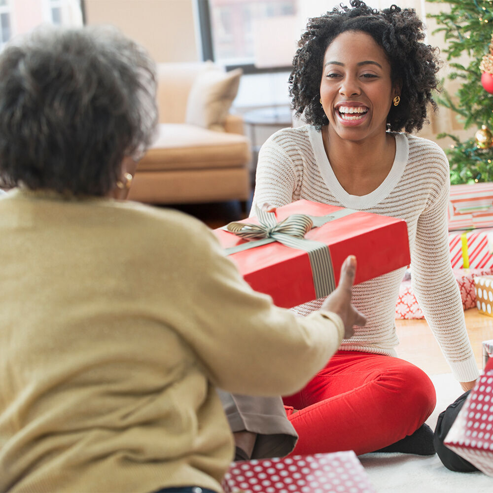 Two people sit on the floor and lovingly give a gift, surrounded by a festive atmosphere.