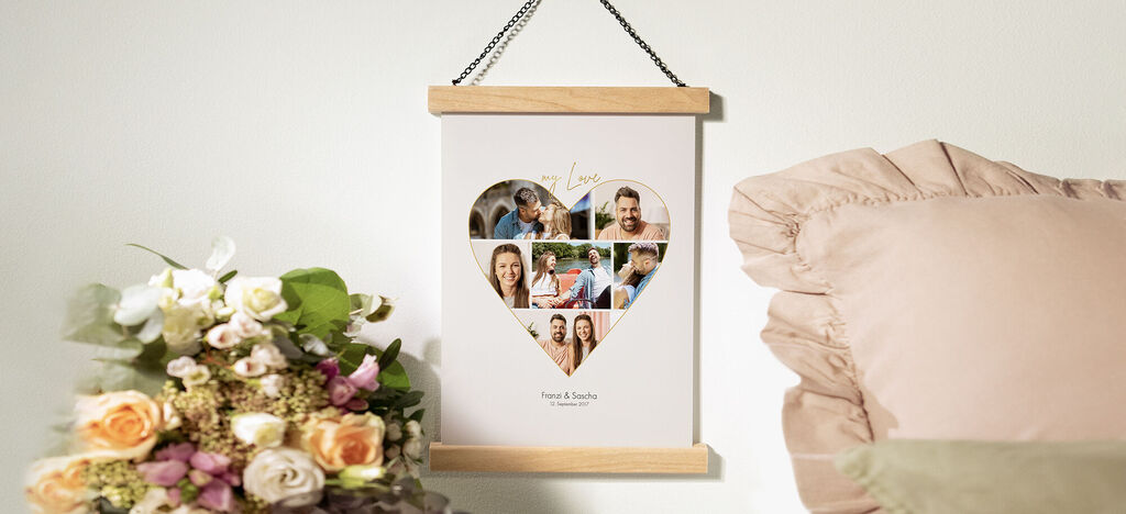 A heart-shaped wall picture with images of happy people. A beautiful flower decoration lies next to it.