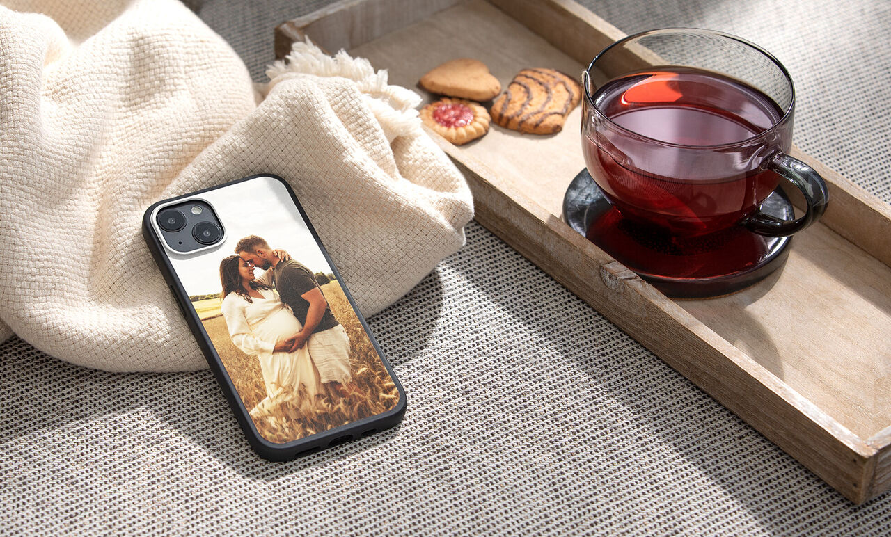 A phone with a photo cover showing a couple in a meadow. Cookies and a cup of tea lie beside the phone.