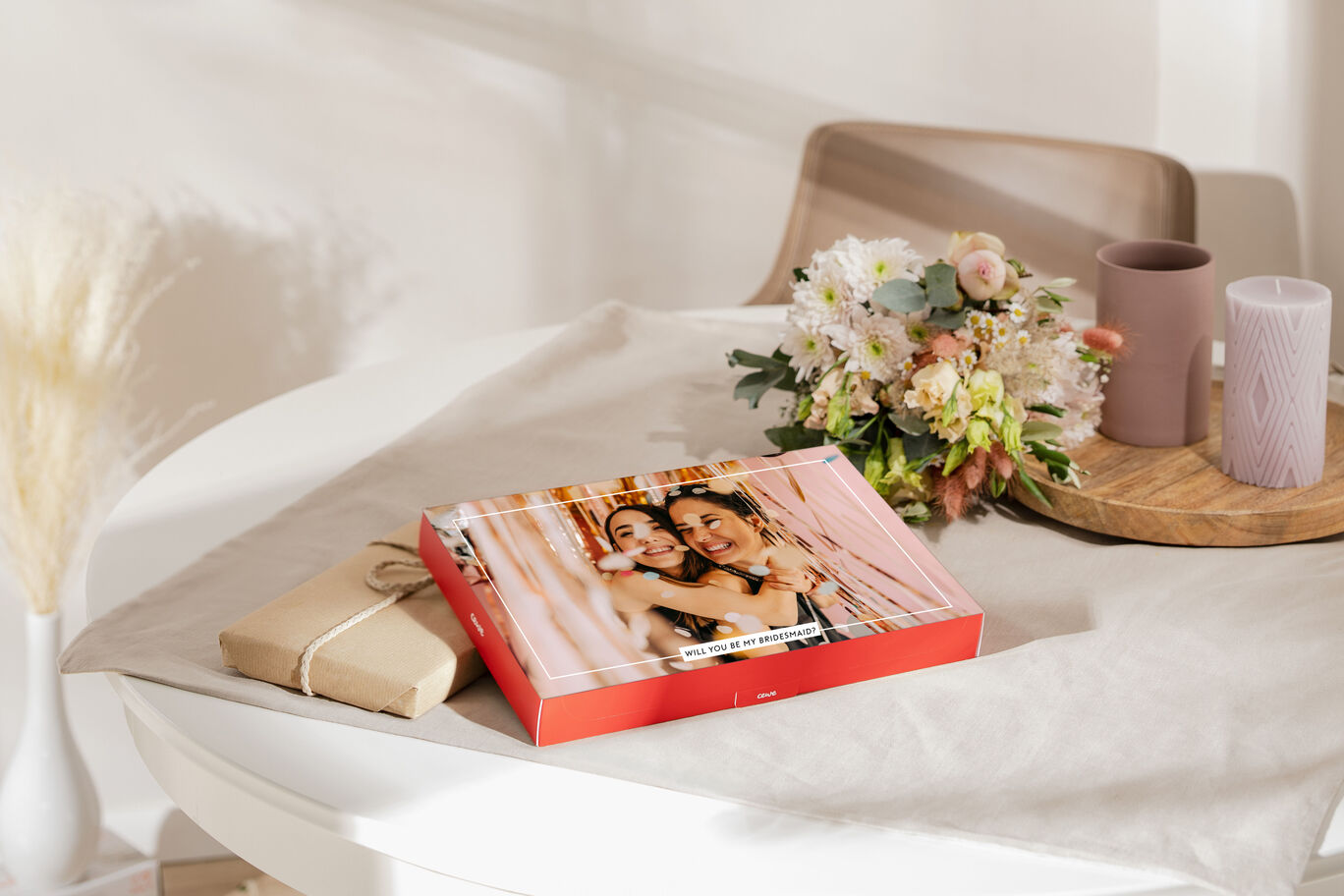 A CEWE photo book on a table, surrounded by flowers and candles. It shows two happy women celebrating.