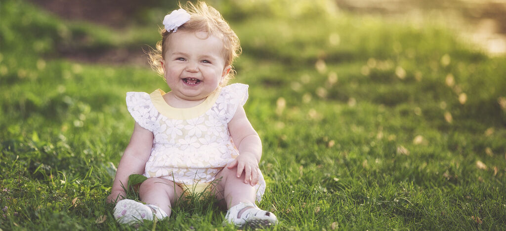 A small child sitting on the green grass enjoying the sun.