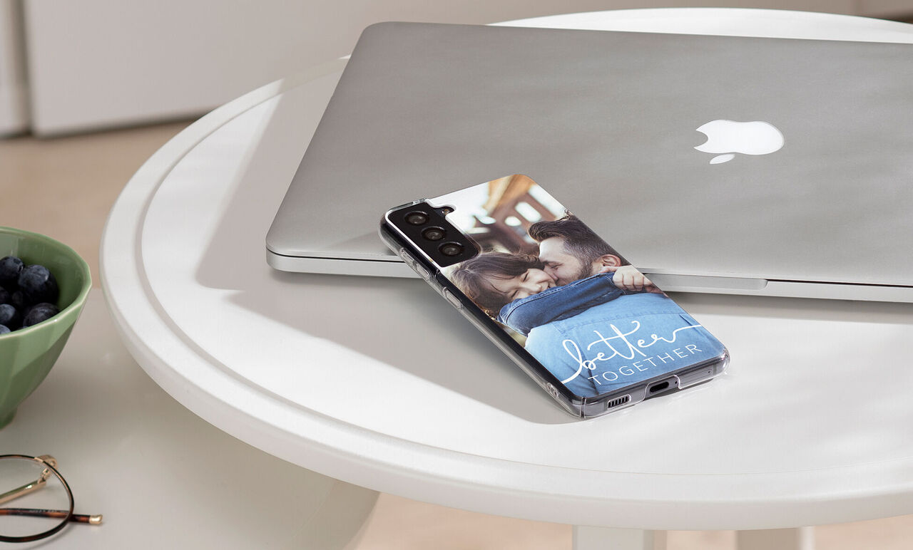 A smartphone with a loving photo of two people embracing, on a table next to a laptop.