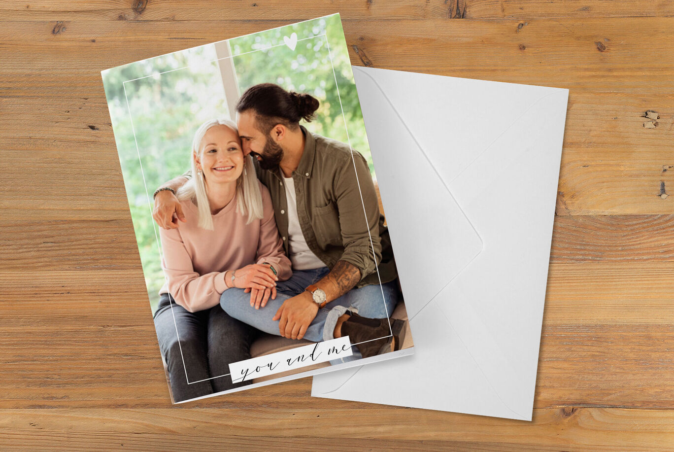 A couple lovingly sits together on a sofa, holding a greeting card. The wall behind them is bright and inviting.