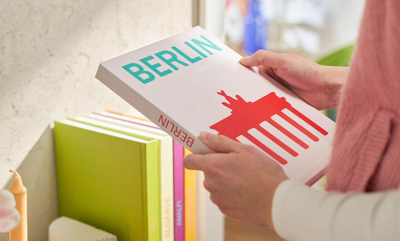 Five photo books with a coffee table book design standing in a modern, colourful living room, every book is designed for a different travel location.