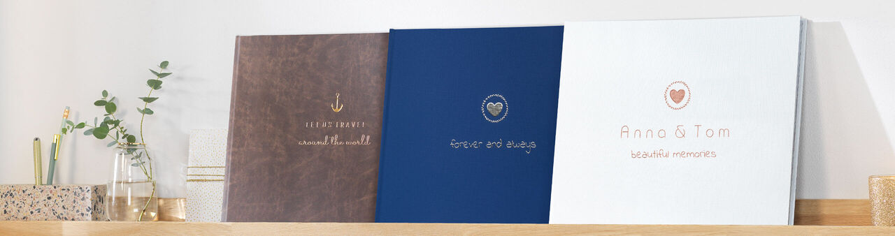 Three beautiful CEWE photo books on a shelf. Different designs in brown, blue and white.