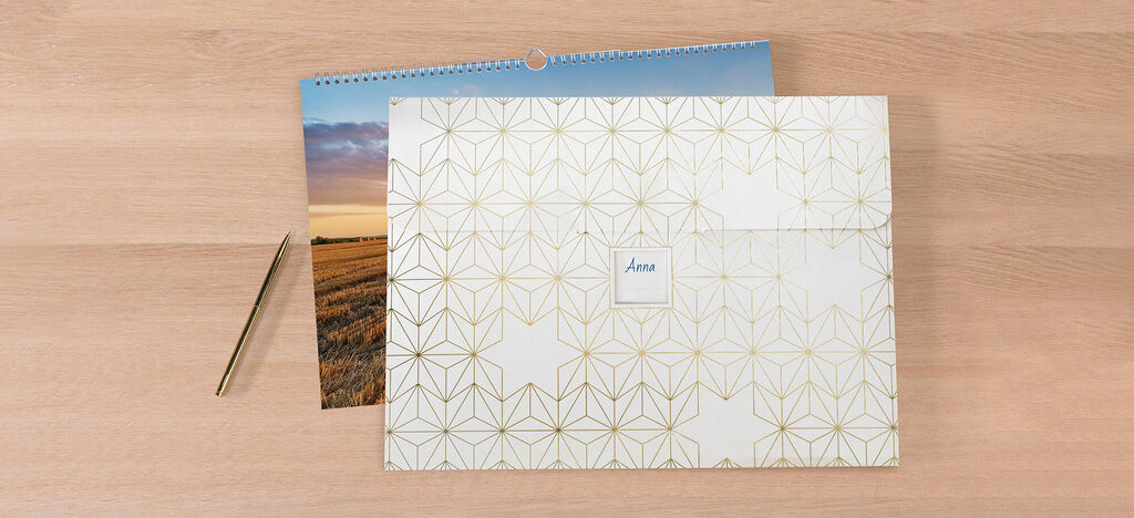 Elegant CEWE greeting cards lie with a calendar on a table. A gold pen is next to them.