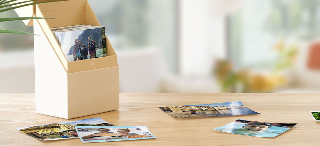 A stylish photo storage container with several photos surrounding it on a table.