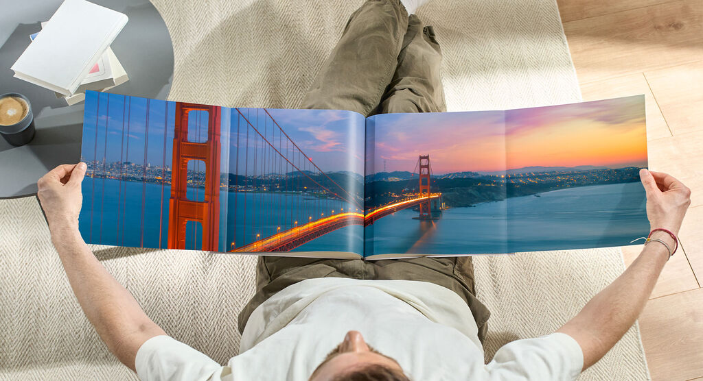 A person sits comfortably on the floor, looking at an open photo book featuring a stunning photo of the Golden Gate Bridge at sunset.