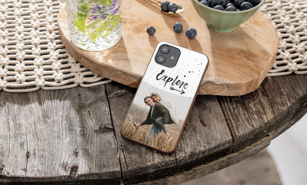 A personalized phone cover on a rustic wooden table with a happy couple in a field.
