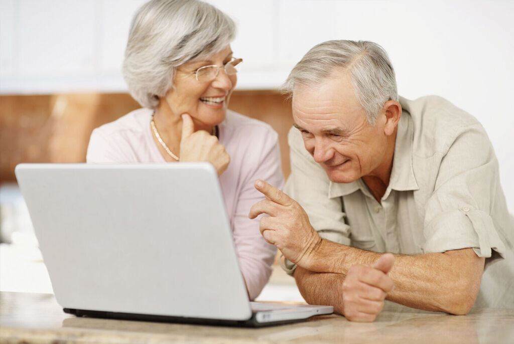 Two older people look at a laptop together and seem to be chatting