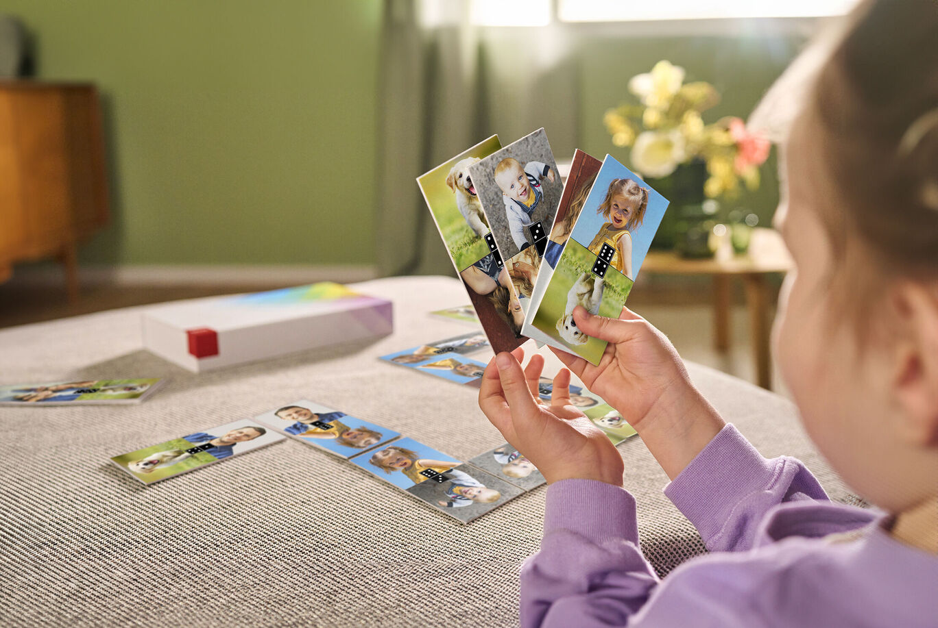 A person holds several photo cards and looks at them joyfully. Flowers and a cozy living room can be seen in the background.