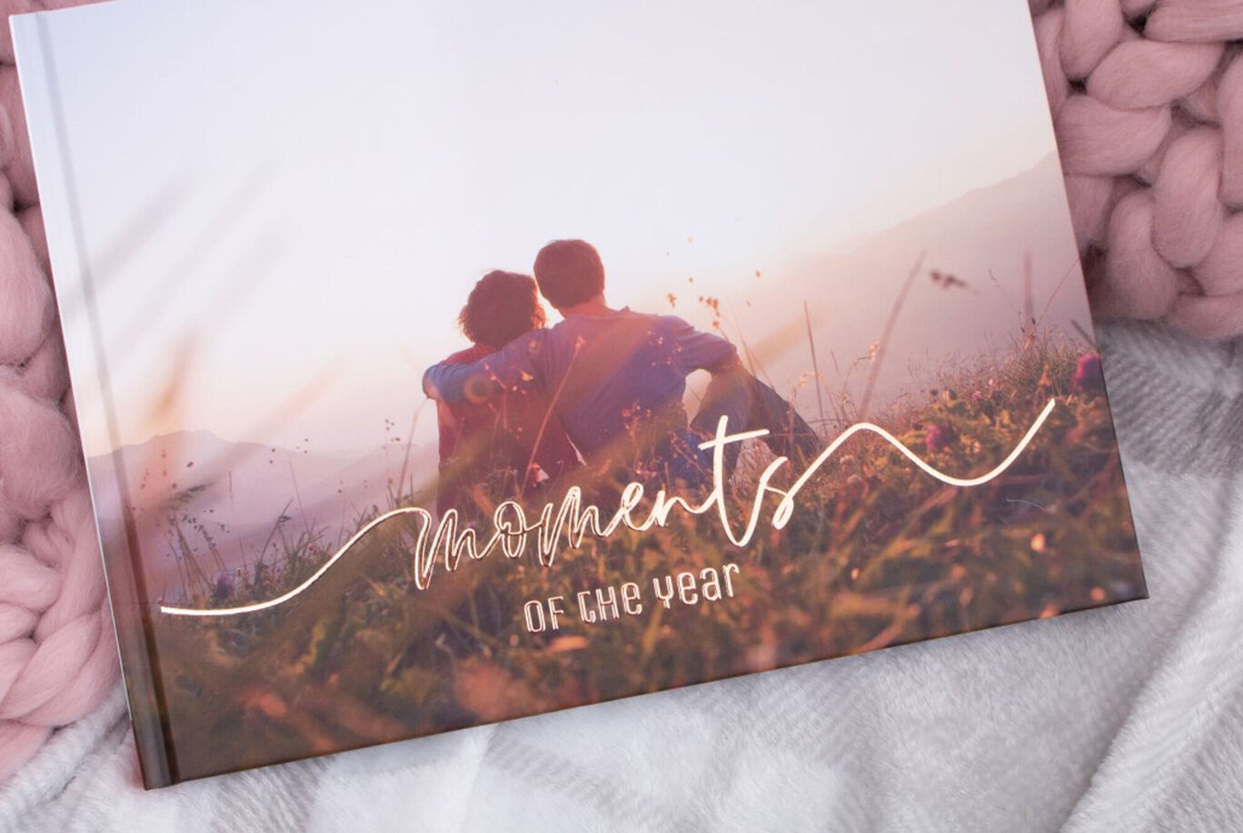 A couple lovingly sits on a meadow enjoying the sunset with their CEWE PHOTO BOOK
