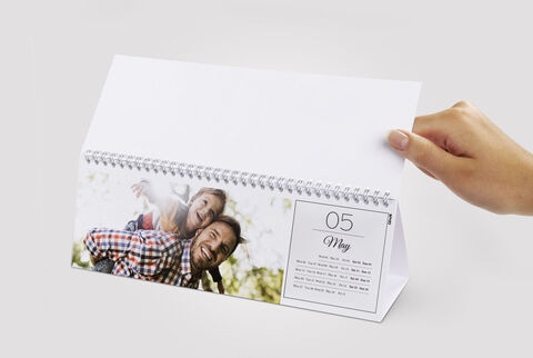 A person flipping through a CEWE photo calendar featuring a cheerful image of two people outdoors.
