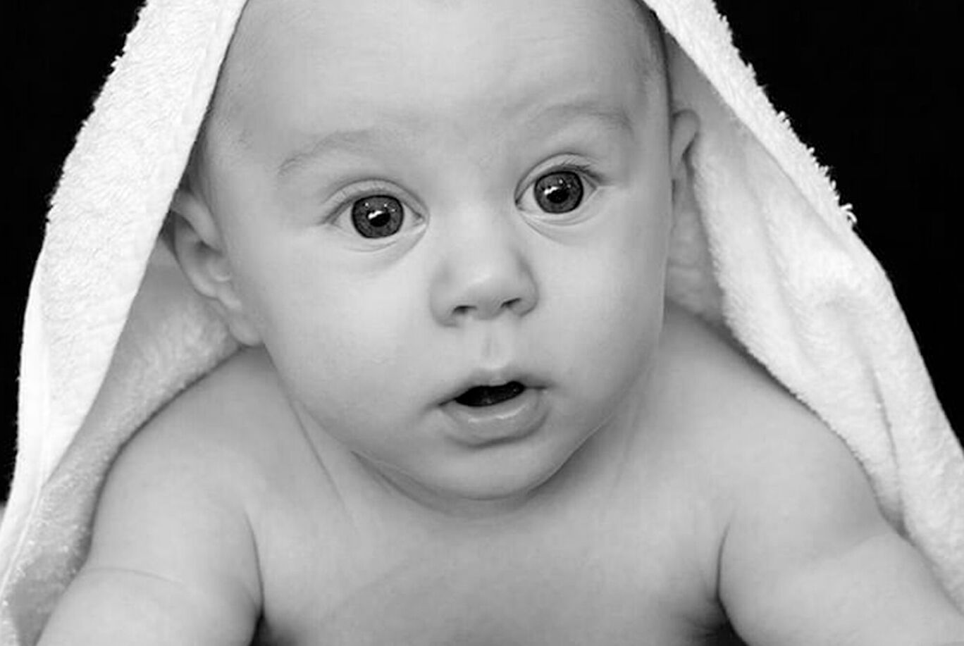 A baby wrapped in a towel looks curiously at the camera