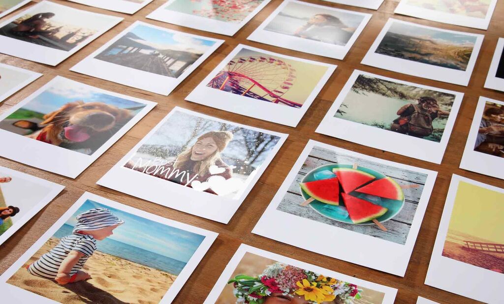 Diverse photo prints arranged on a wooden table, showing happy people and beautiful moments like vacations and colorful fruits.