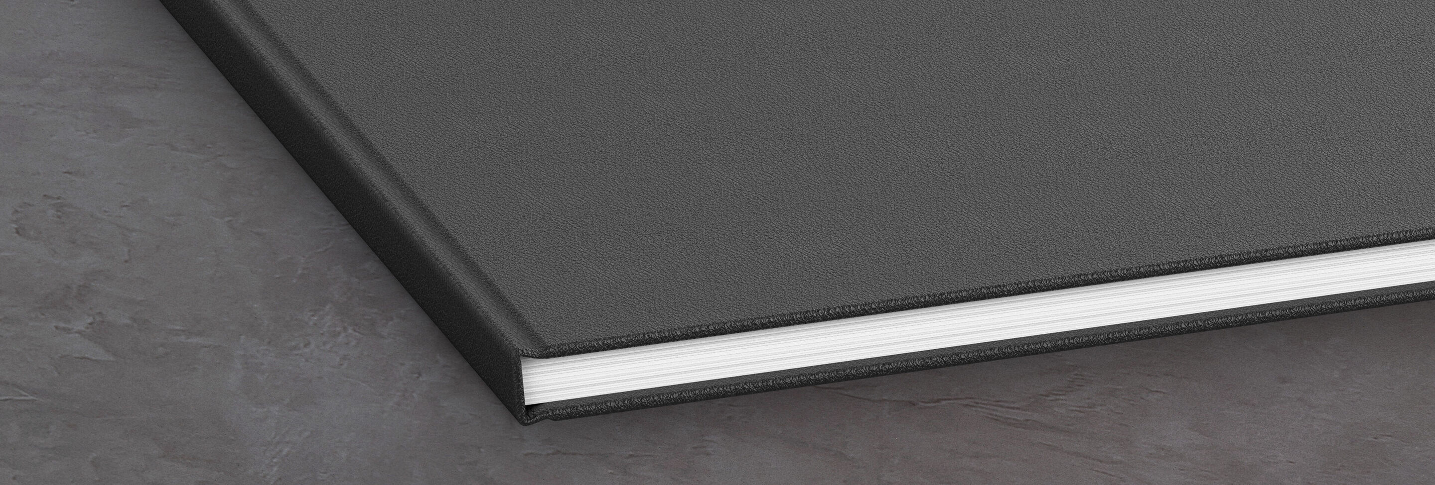 A closed, black photo book lying on a gray surface.