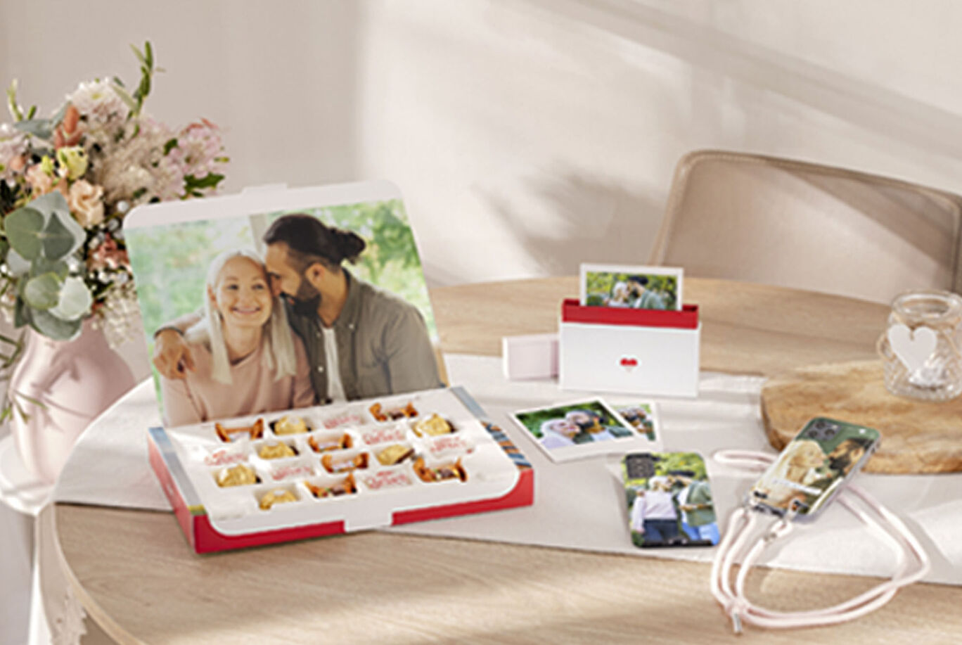 A creative gift box with photo contents on a table, surrounded by flowers and photos.