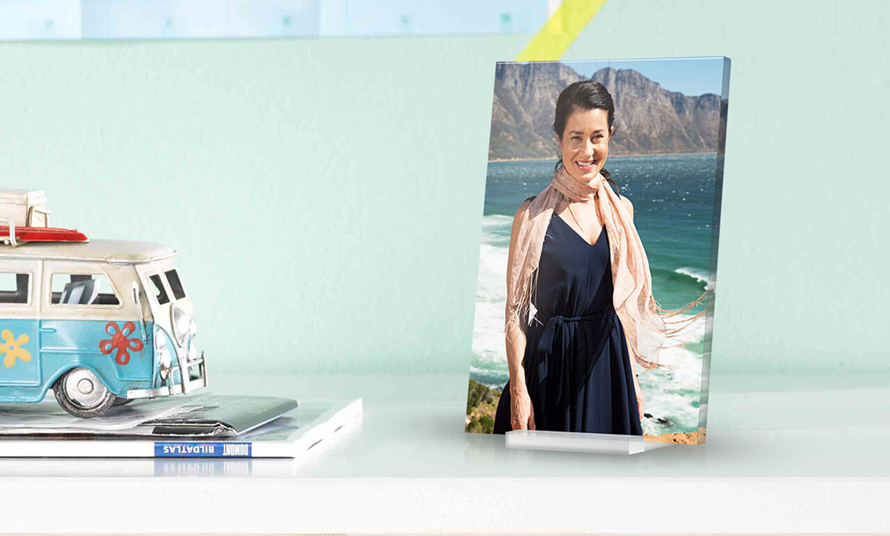 A person stands on the beach looking at the sea and mountains in the background. They wear an elegant dress with a scarf.