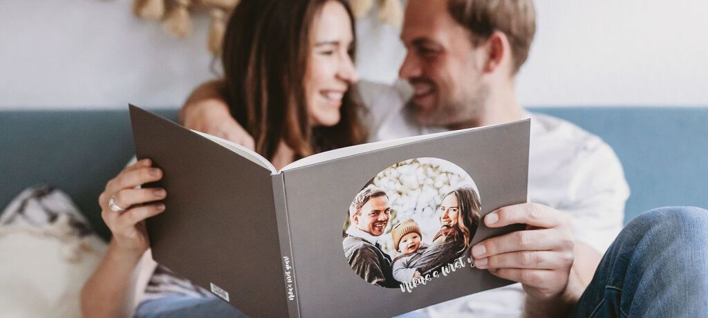 A couple sits together looking at a CEWE photo book. They laugh and enjoy their shared memories.