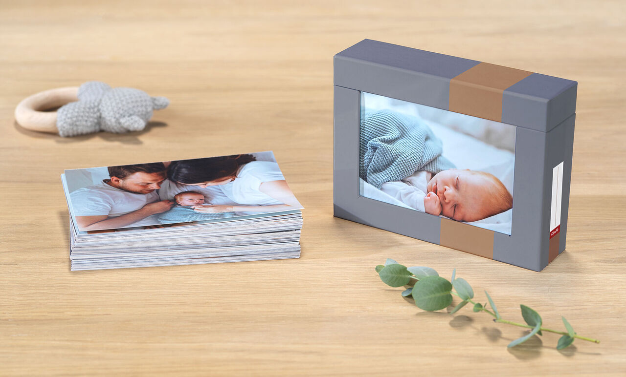 CEWE photo book with photos of a newborn and family on a wooden table, alongside a box with a picture of the sleeping baby.