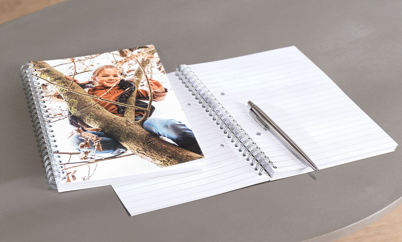 A CEWE photo book on a table with a children's photo and a blank notebook.