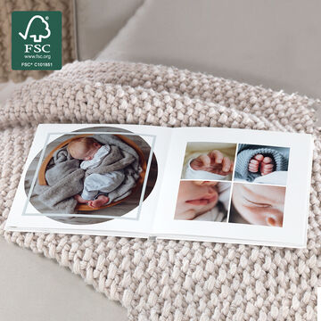 An open CEWE photo book with baby photos on a cozy living room table, softly knitted.