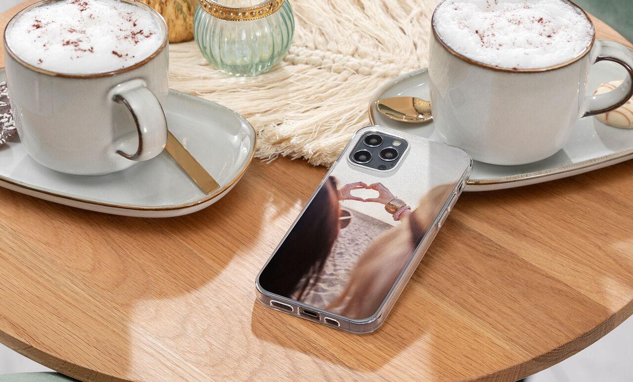 A phone with a light image on a table between two cups of cocoa.