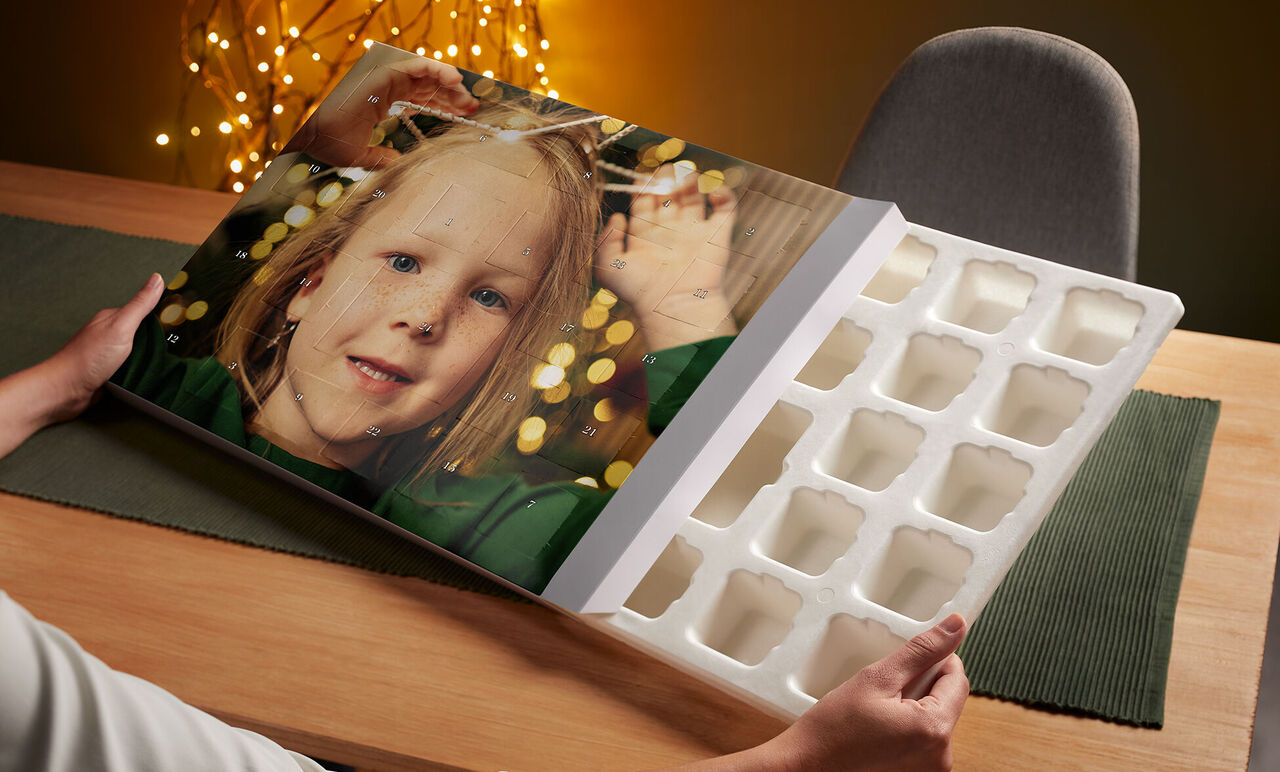 A person holds an open CEWE photo book with colorful lights and a photo on the cover.