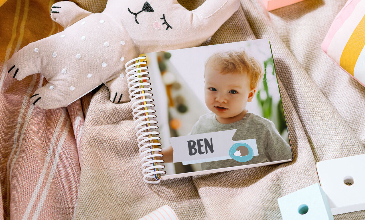 A cheerful photo book lies on a colorful blanket, surrounded by toys and soft textiles.