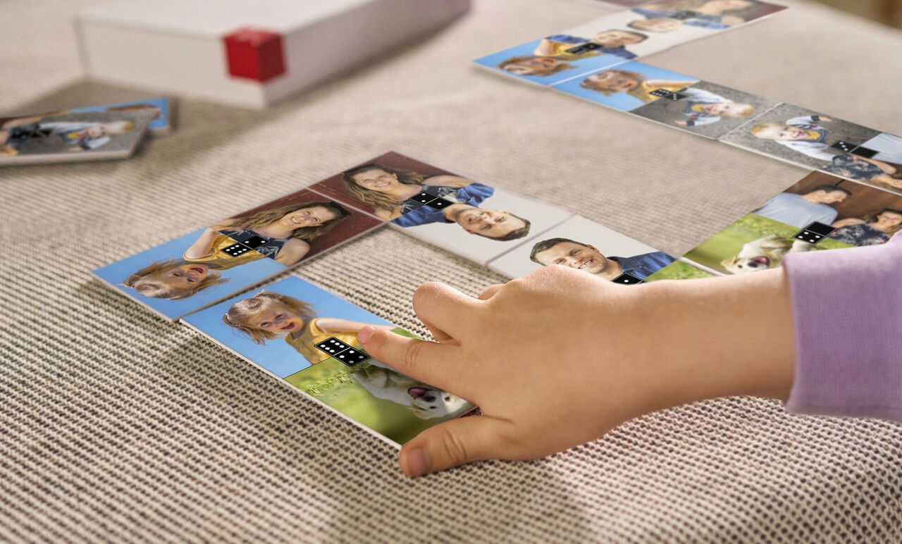A child plays with personalized dominoes on a table showing photos of friends and family.