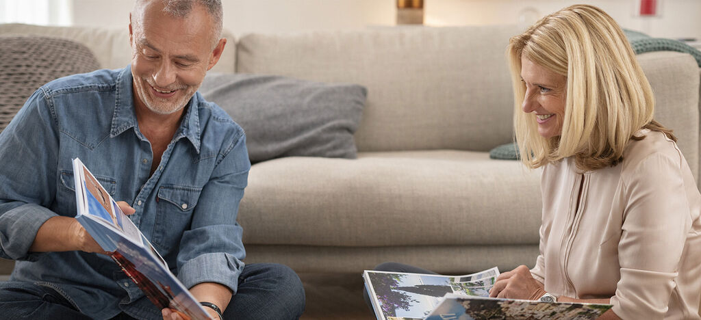 Two people look at a photo book together on the floor. One person holds a photo book uphigh.