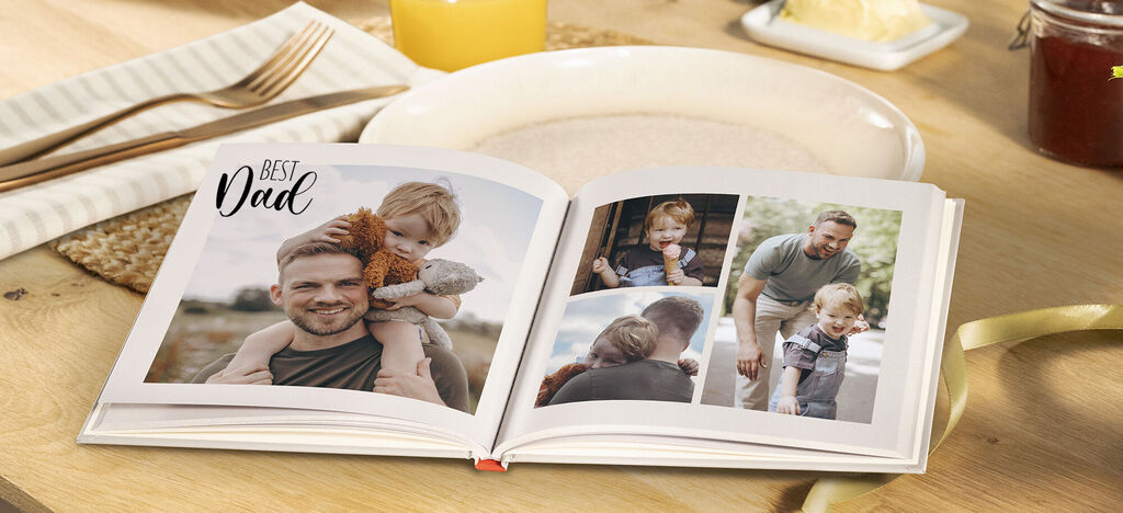 An open CEWE PHOTOBOOK with images of a father and child on a wooden table.