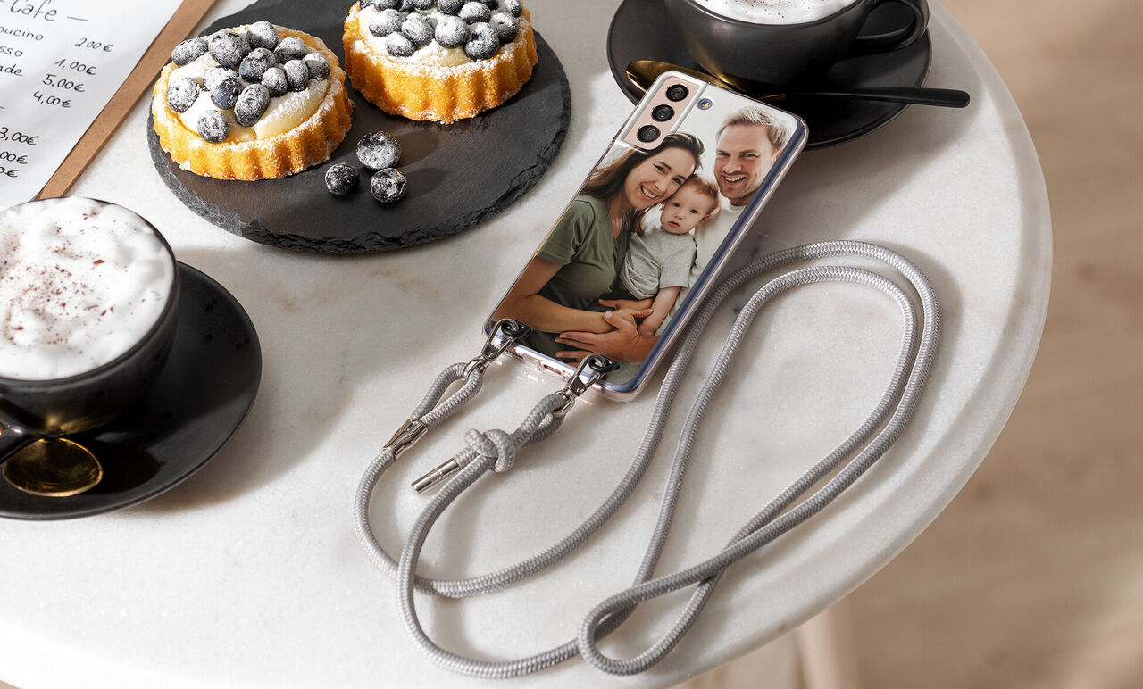 A smartphone with a photo motif on a table beside a coffee cup and two cakes.