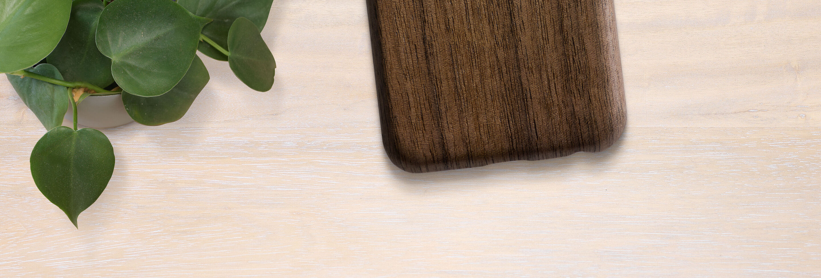 Wood-colored phone case on a light table with a plant
