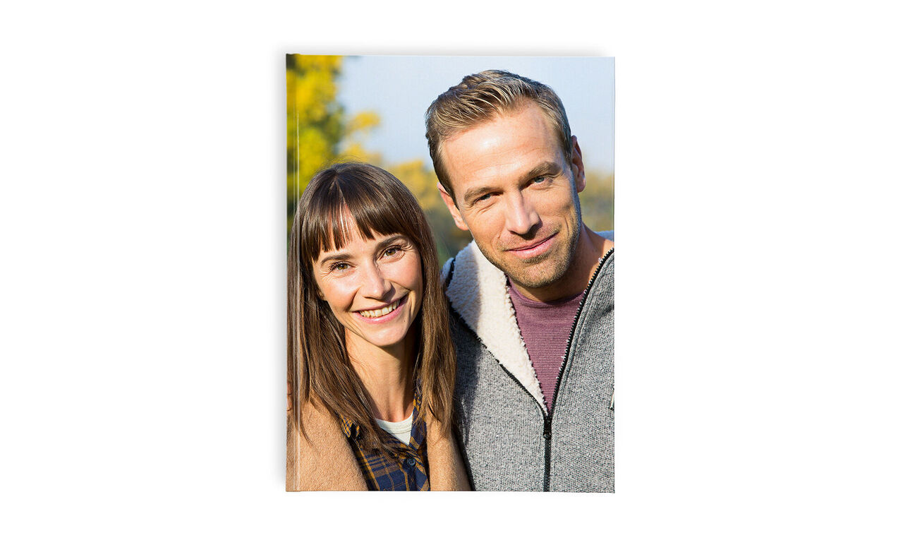 Two people smile in nature, a woman with long hair and a man with older styling.