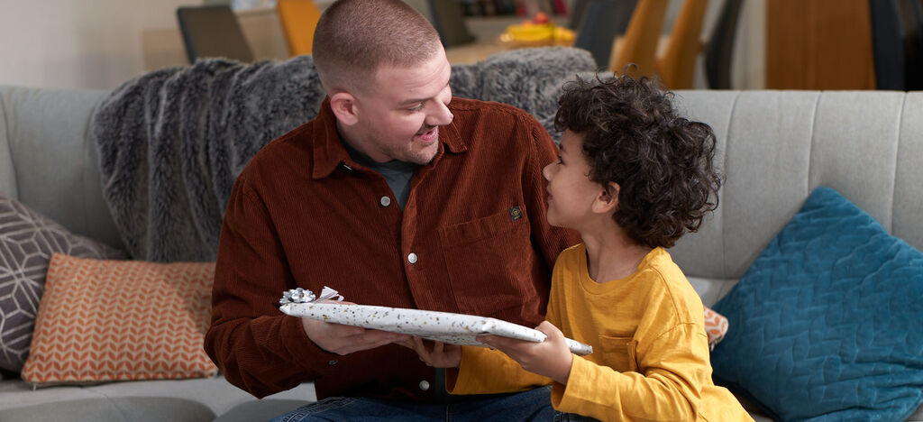 A child hands a gift to an adult on a cozy sofa. The atmosphere radiates joy and togetherness.