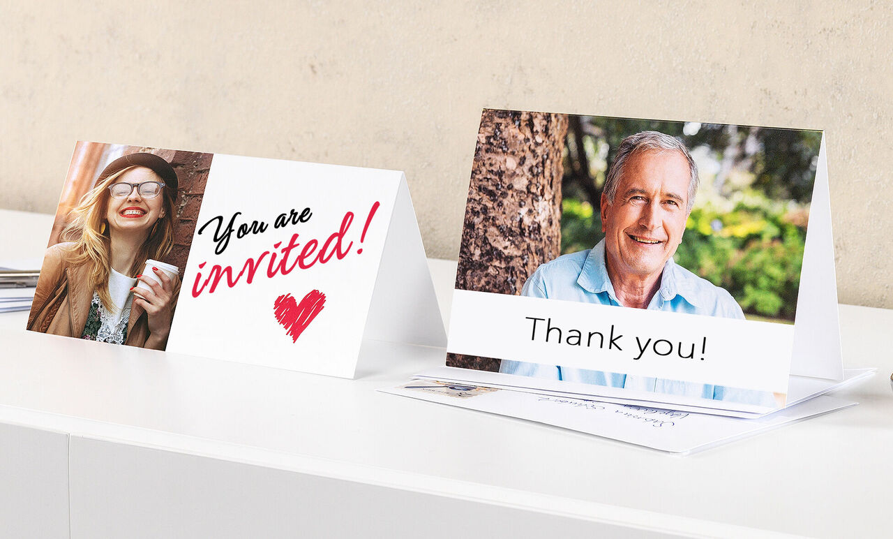 Two inviting greeting cards on a table. One card shows the text 'You are invited!' in colorful letters, the other says 'Thank you!' under a picture.