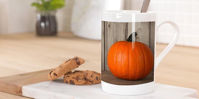 A creative mug with an orange pumpkin and a cookie accompaniment on an elegant table.