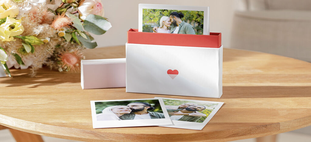 A lovely gift box with photos, surrounded by blooming flowers, on a wooden table.