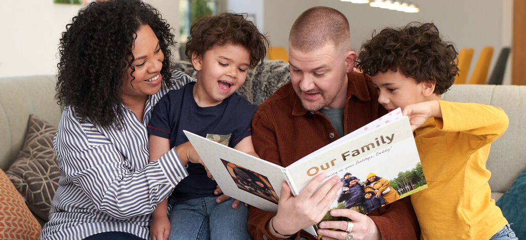 A family sits together on a sofa reading a photo book titled 'Our Family'. The atmosphere is relaxed and joyful.