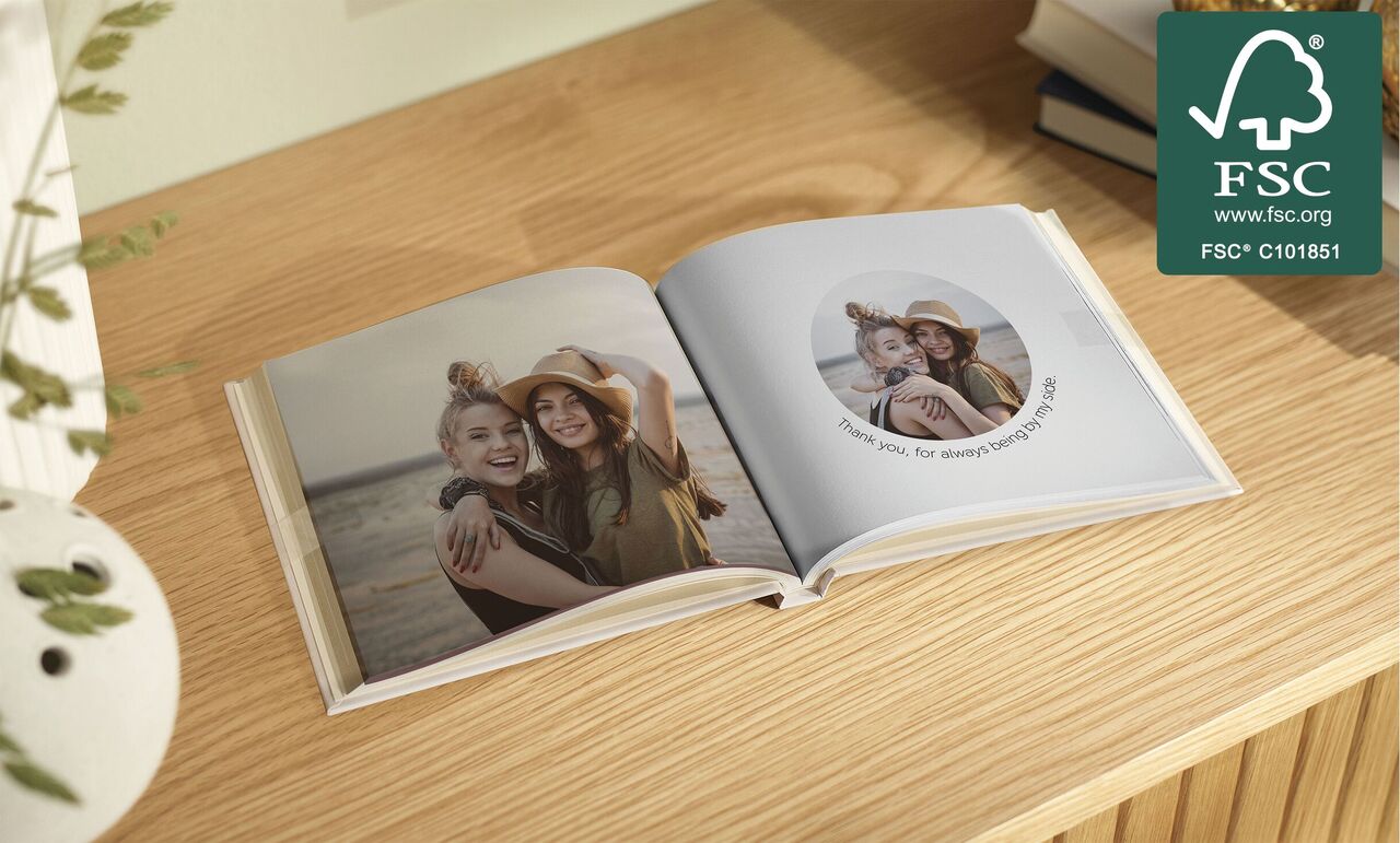 An opened CEWE PHOTO BOOK on a wooden table with joyful memories and two people on one page.