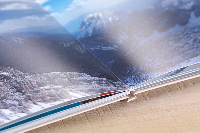 An open photo book displays a beautiful mountain landscape on the left side, with large pages in vibrant colors.